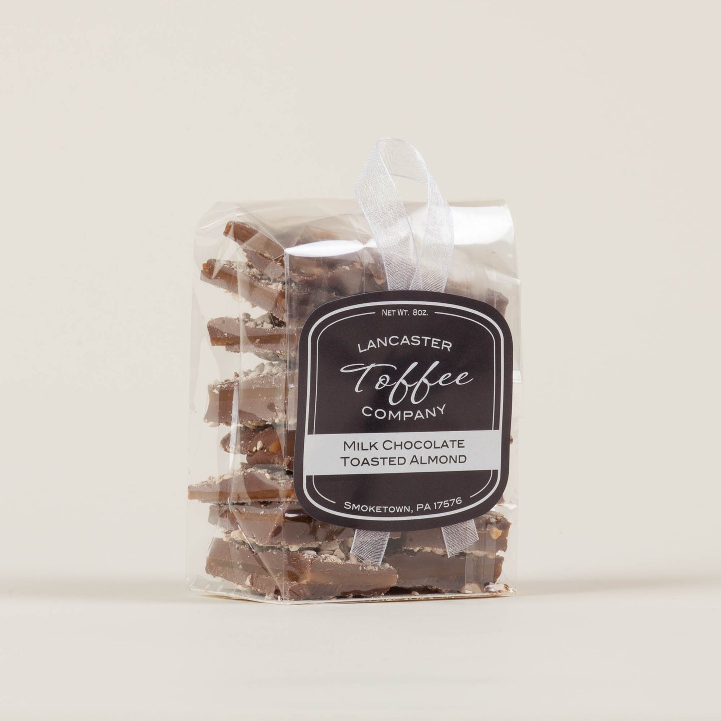 Eight-ounce bag of Lancaster Toffee Co. Almond Milk Chocolate Toffee on a light background, English-style toffee with milk chocolate and almond pieces made in Lancaster, PA.