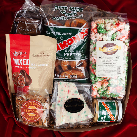 Festive Favorites holiday gift box on a red velvet background, filled with chocolate pretzels, peppermint bark, Wilbur Buds, seasonal popcorn, hand-rolled pretzels, and peppermint stroopwafel crumble from Lancaster, PA.