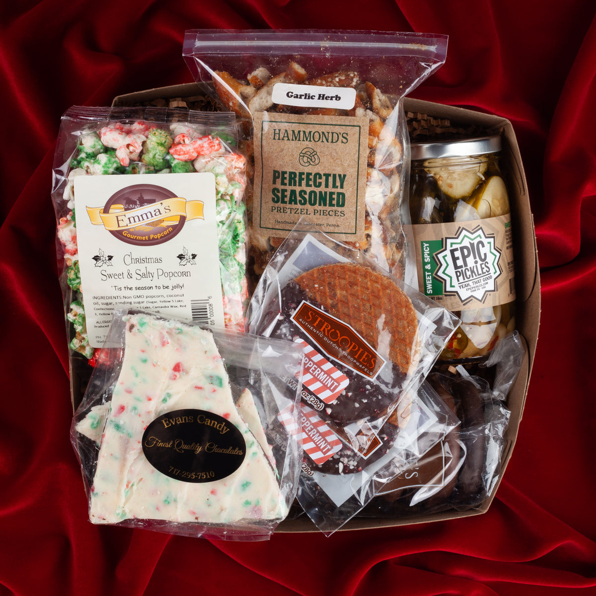 Holiday Cheer gift box on a red velvet background, filled with seasonal popcorn, peppermint bark, festive pretzels, peppermint stroopwafels, and sweet and spicy pickles from Pennsylvania makers.