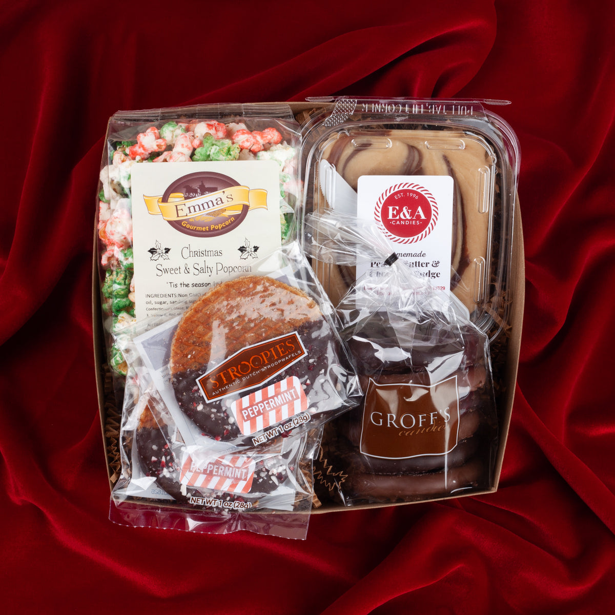 Holiday Nosh gift box on a red velvet background, filled with seasonal popcorn, chocolate pretzels, chocolate nut fudge, and peppermint stroopwafels from Lancaster, PA.