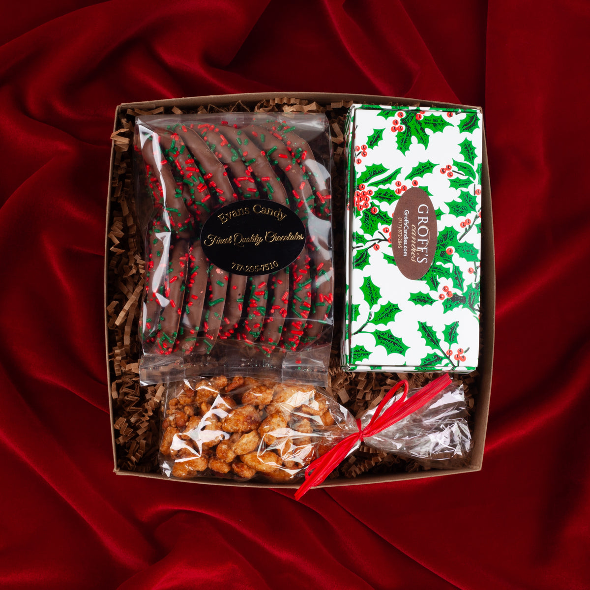 Yuletide Sweets holiday gift box on a red velvet background, filled with festive assorted chocolates, Christmas sprinkle pretzels, and toffee butter cashews from Pennsylvania makers.