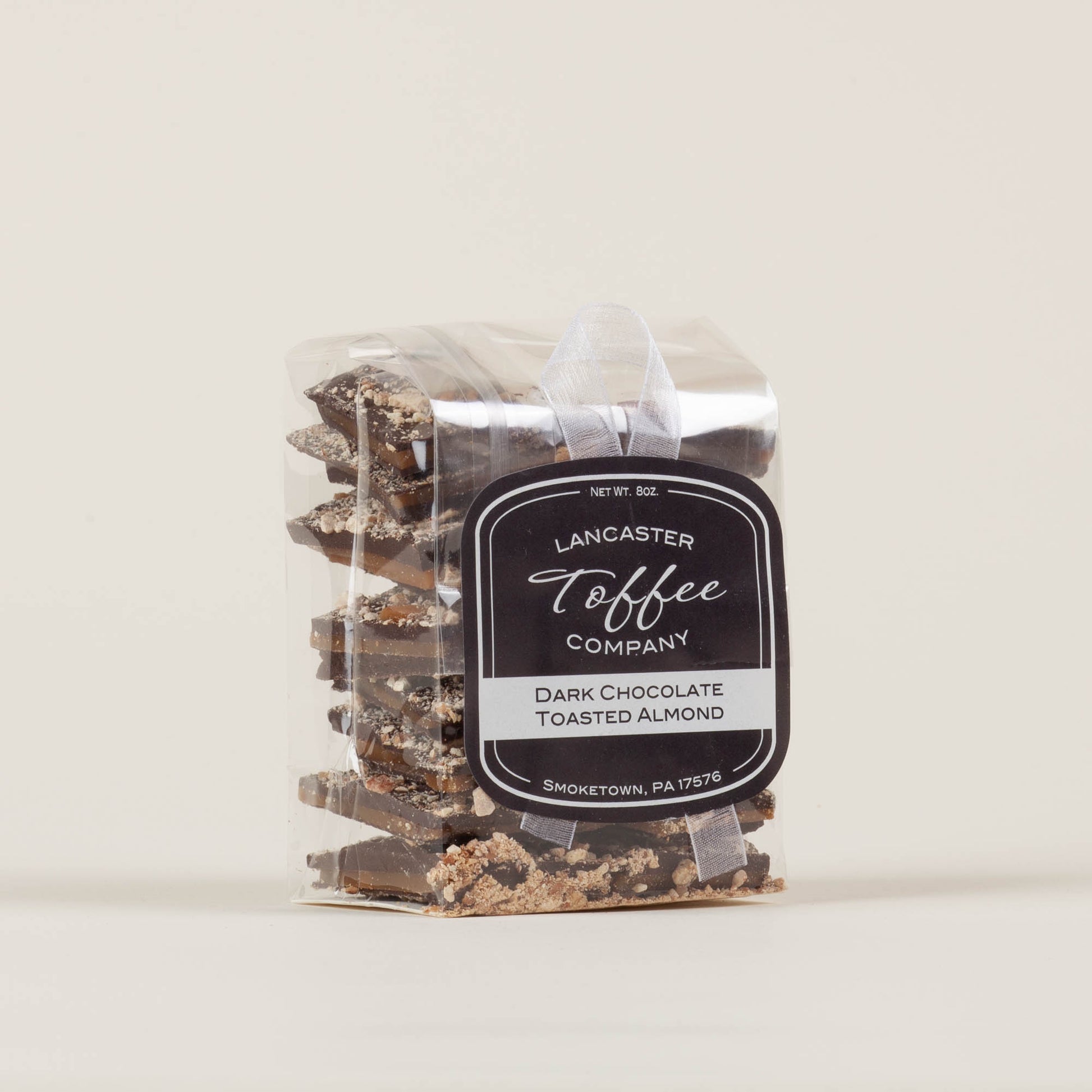 Eight-ounce bag of Lancaster Toffee Co. Almond Dark Chocolate Toffee on a light background, English-style toffee with dark chocolate and almond pieces made in Lancaster, PA.