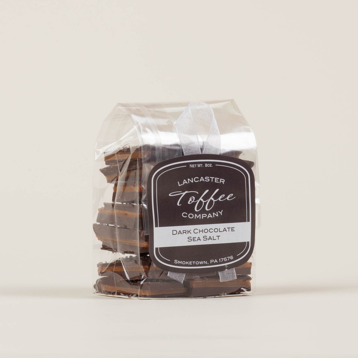 Eight-ounce bag of Lancaster Toffee Co. Sea Salt Dark Chocolate Toffee on a light background, English-style toffee with dark chocolate and sea salt made in Lancaster, PA.